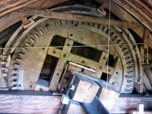 Inside the mill's cap. While the rest of the structure is stationary, the cap can be turned into the wind when needed. The sails are affixed to the cast iron axle and drive the giant 'brake wheel'. Its name is derived from the curved wooden pieces around the wheel that act as a brake.